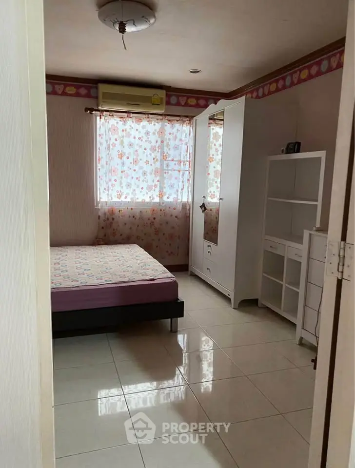Cozy bedroom with floral curtains and tiled flooring, featuring a bed and wardrobe.