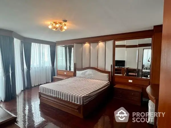 Spacious master bedroom with polished hardwood floors, large windows draped in elegant curtains, and mirrored wardrobe doors reflecting natural light.