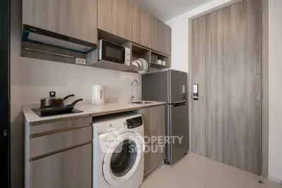 Modern kitchen with washing machine, microwave, and fridge in sleek wood cabinetry.