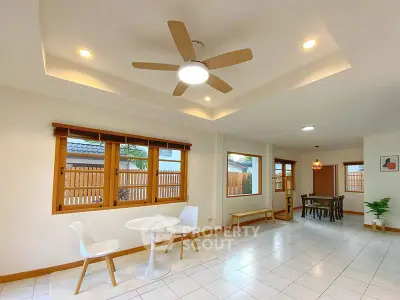Spacious living room with modern ceiling fan and dining area, featuring large windows and stylish decor.