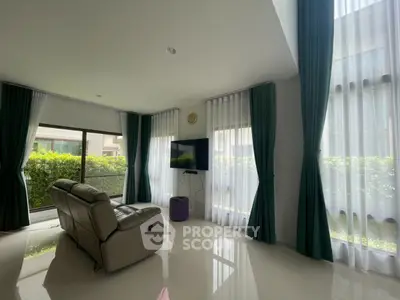 Spacious living room with modern recliner and large windows offering lush garden views.