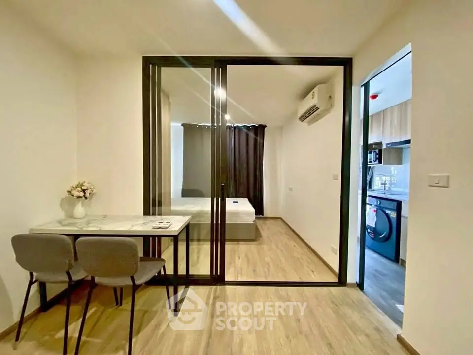 Modern apartment interior with glass partition, dining area, and view into bedroom and kitchen.