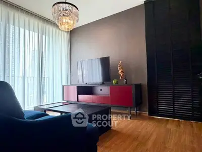 Modern living room with stylish chandelier and sleek furniture, featuring a large TV and floor-to-ceiling windows.