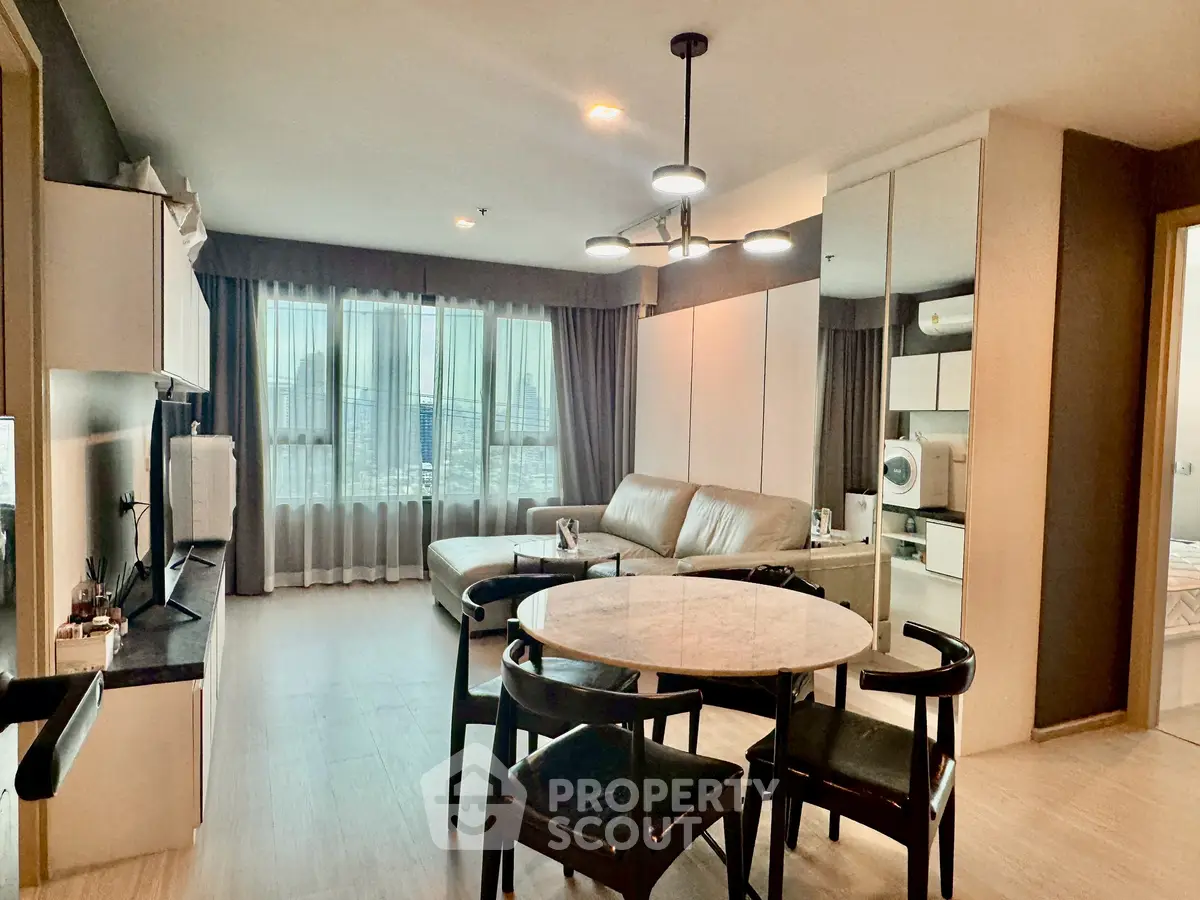 Modern living room with dining area and city view, featuring sleek furniture and natural light.