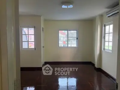 Spacious room with polished wooden floors and large windows in a bright home.