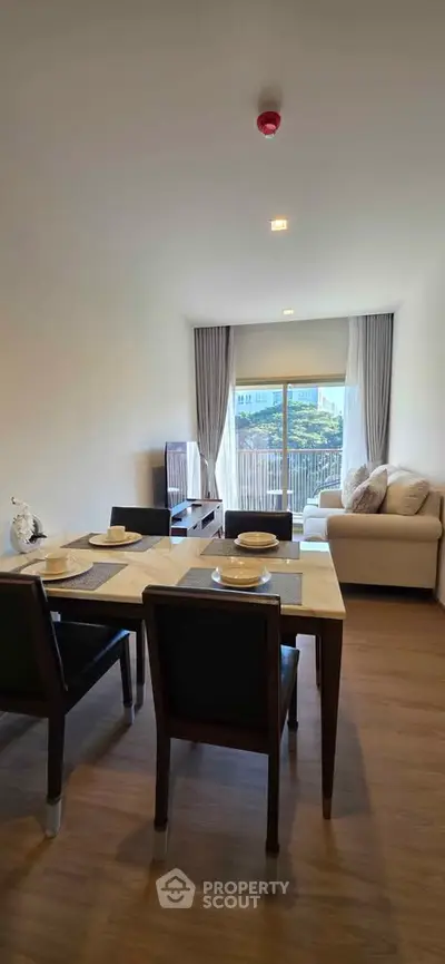 Modern living room with dining area and balcony view, featuring elegant decor and natural light.