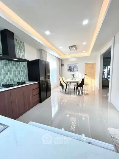 Modern kitchen with sleek design and dining area, featuring stylish lighting and glossy tiles.
