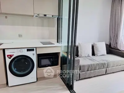 Modern apartment with compact kitchen and cozy living area featuring washing machine and microwave.