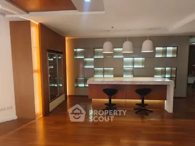 Modern kitchen with stylish lighting and wooden flooring, featuring a sleek island and contemporary bar stools.