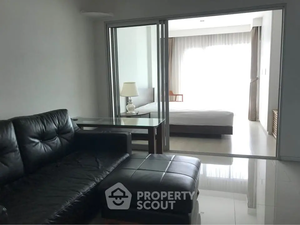 Modern apartment with sleek black leather sofa and bright bedroom view.