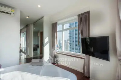 Bright bedroom with city view, large window, and wall-mounted TV in modern apartment.