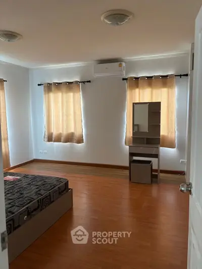 Spacious bedroom with wooden flooring and natural light