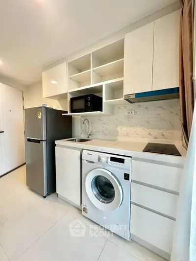 Modern kitchen with washing machine, fridge, and microwave in compact layout.