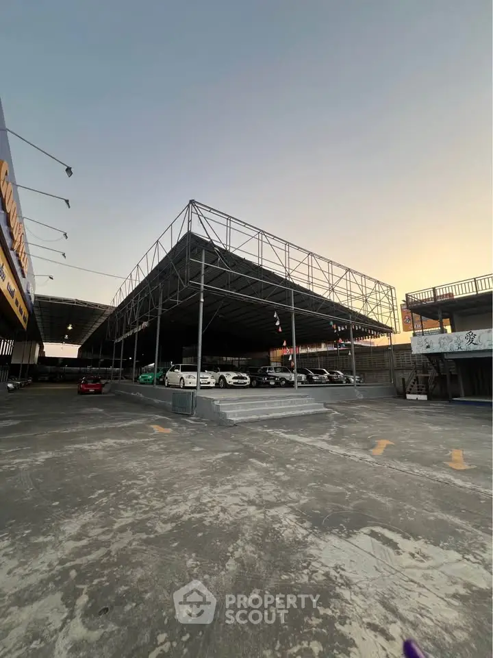 Spacious commercial parking area with steel structure and multiple cars at sunset.