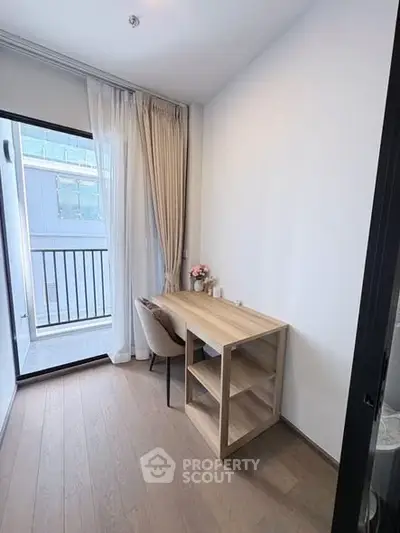 Cozy study room with wooden desk and chair, adjacent to a small balcony with glass door.