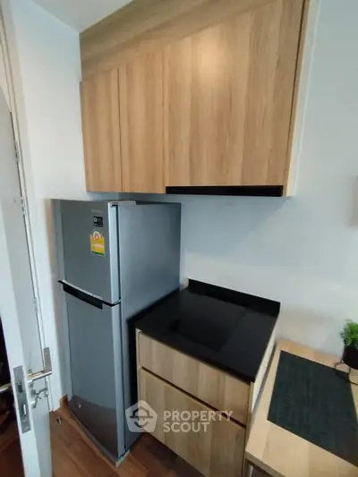 Modern compact kitchen with sleek wooden cabinets and stainless steel fridge
