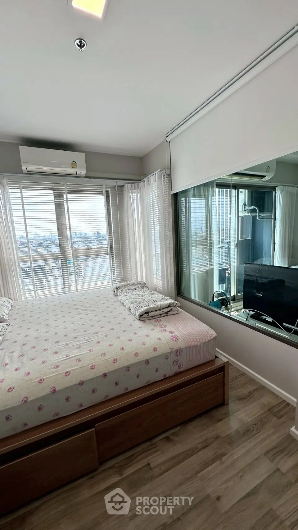 Modern bedroom with large windows offering stunning city views, featuring sleek wooden flooring and contemporary decor.