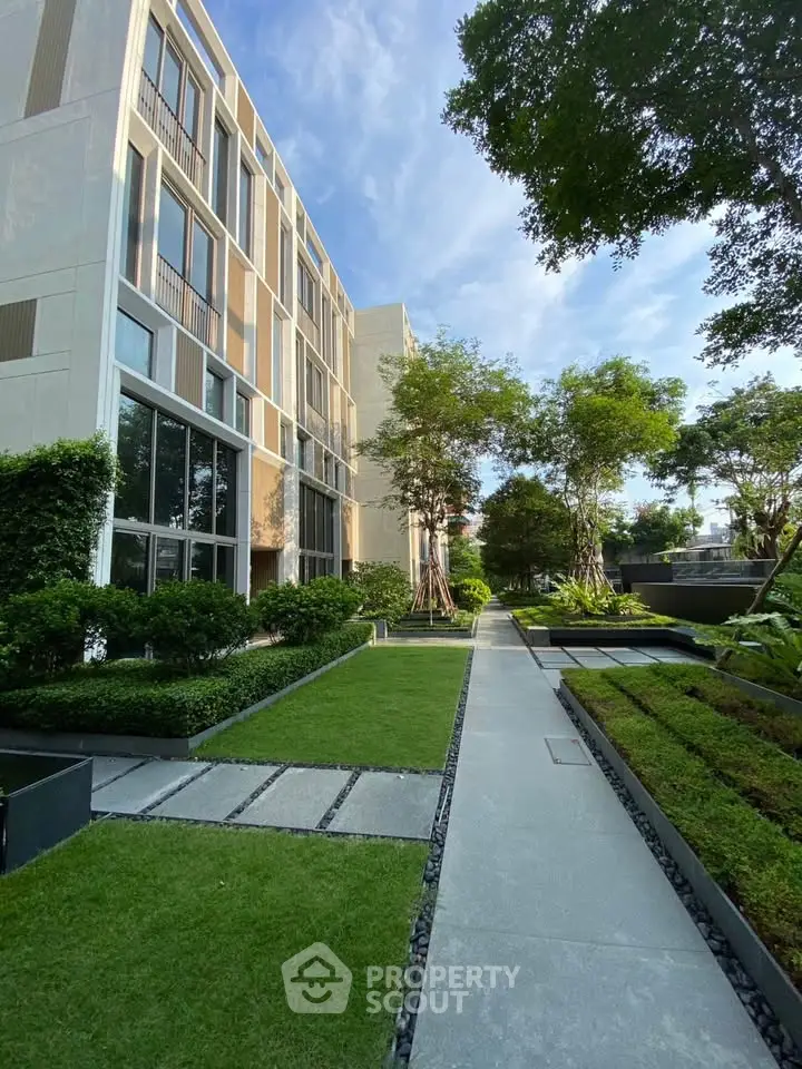 Modern building exterior with lush garden and pathway under clear blue sky.