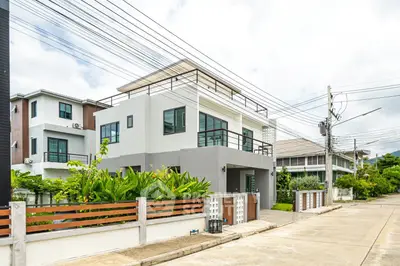 Modern two-story house with rooftop terrace and lush greenery in suburban neighborhood.