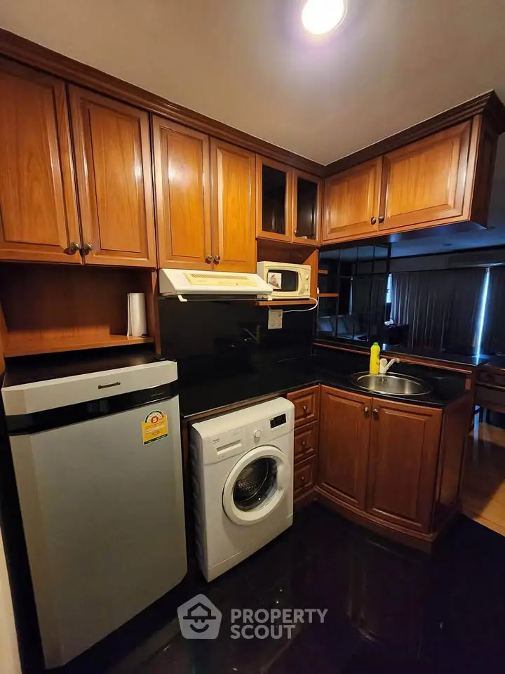 Charming kitchen with wooden cabinets, washing machine, and compact fridge in cozy apartment.