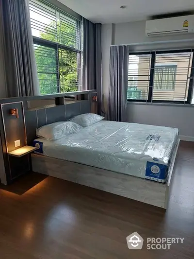 Spacious bedroom with large windows, natural light, and modern design, featuring a new bed and stylish wooden flooring.