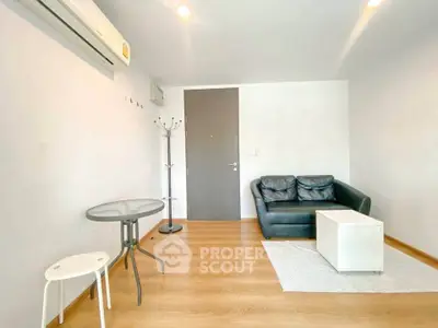Modern living room with sleek black sofa, glass table, and wooden flooring.