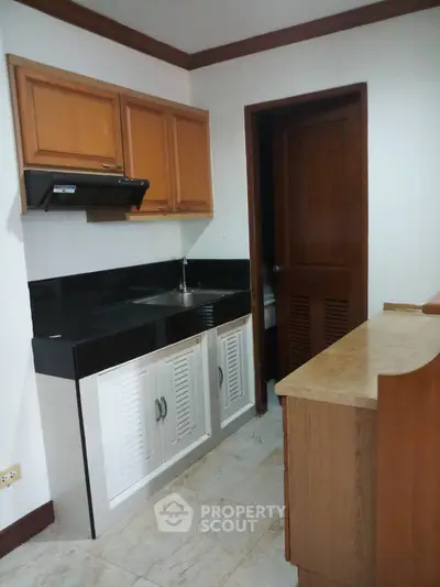 Compact kitchen with wooden cabinets and black countertops in cozy apartment