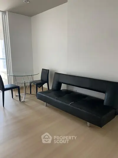 Modern minimalist living room with sleek black sofa and glass dining table.