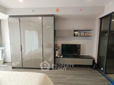 Modern bedroom with sleek wardrobe and entertainment unit, featuring stylish decor and ample natural light.