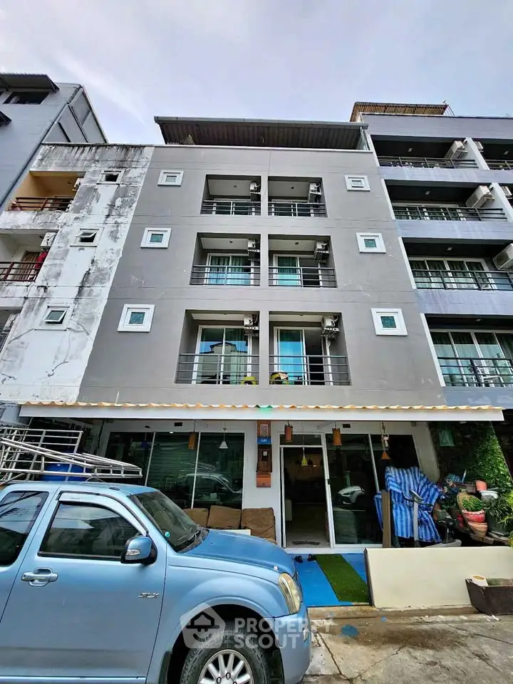 Modern multi-story apartment building with balconies and parking area.