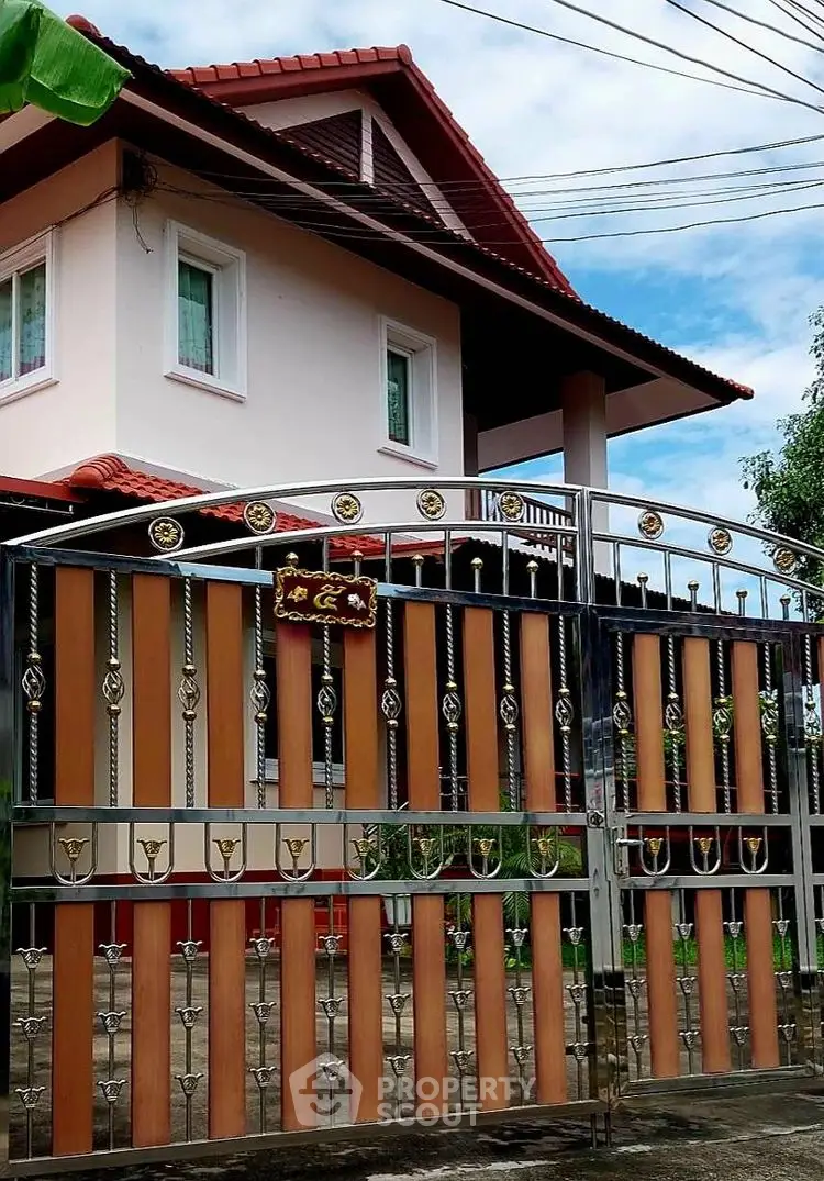 Charming two-story house with decorative gate and lush surroundings.