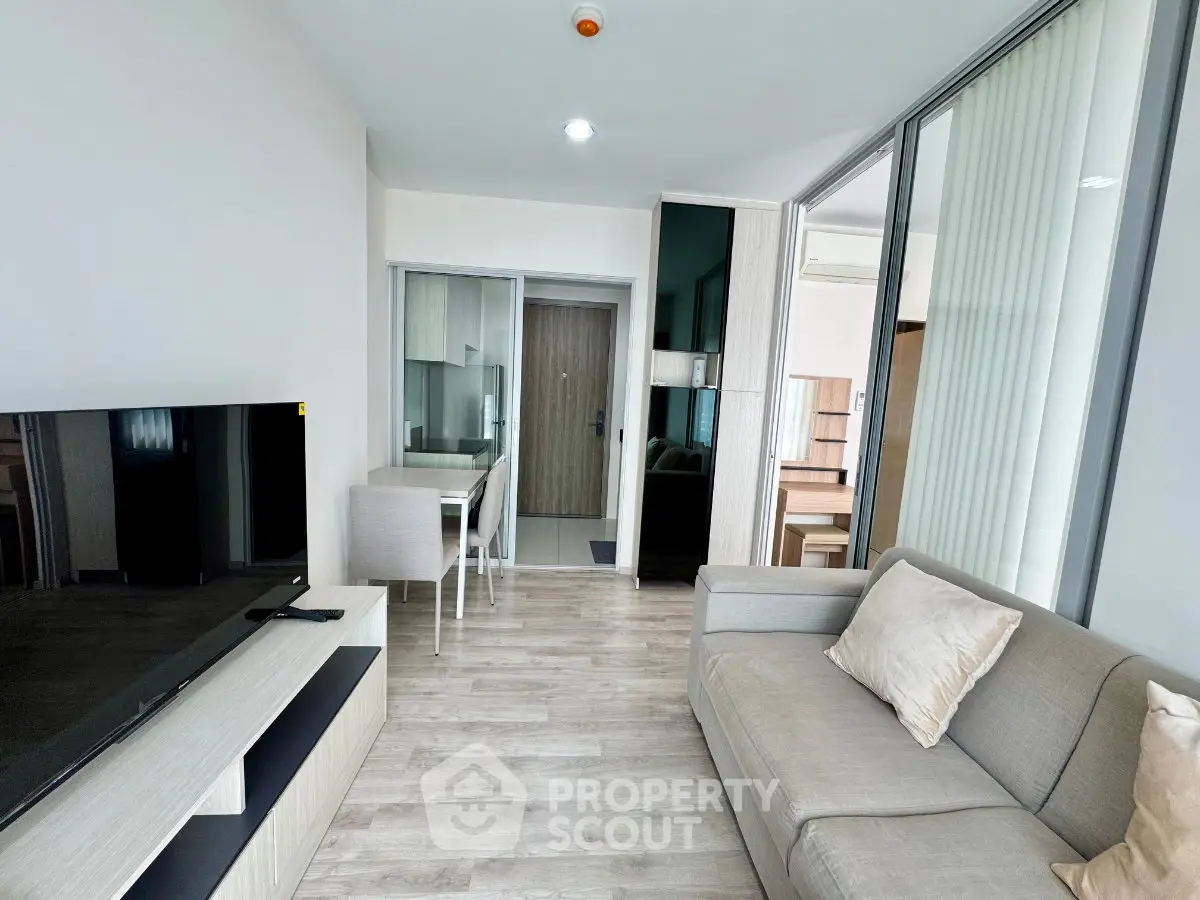 Modern living room with sleek furniture and open layout, featuring a large TV and stylish decor.