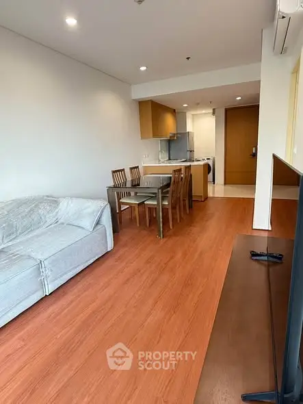 Spacious living room with modern open kitchen and dining area, featuring wooden flooring and cozy sofa.