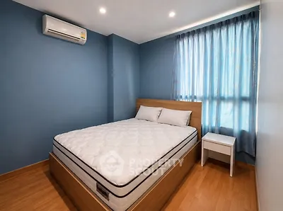Modern bedroom with blue walls, wooden flooring, and natural light from a large window.