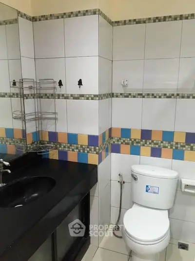 Modern bathroom with colorful tile accents and sleek black countertop.
