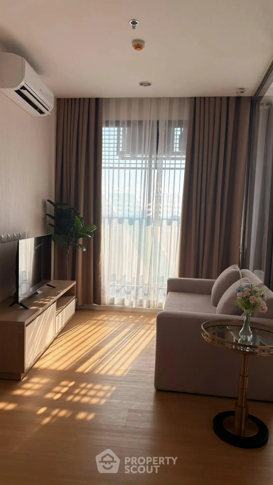 Cozy living room with natural light, modern sofa, and TV setup in a stylish apartment.