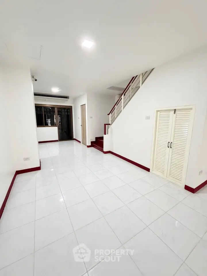 Spacious white-tiled living room with staircase and air conditioning, perfect for modern family living.