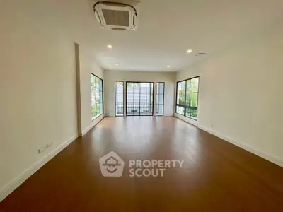 Spacious empty living room with large windows and wooden flooring.
