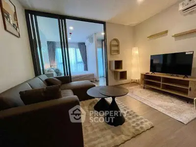 Modern living room with cozy seating and TV, adjacent to a stylish bedroom with natural light.
