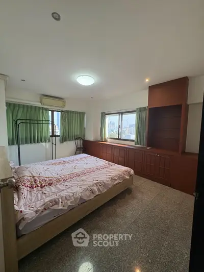 Spacious bedroom with city view and ample natural light, featuring built-in storage and cozy decor.