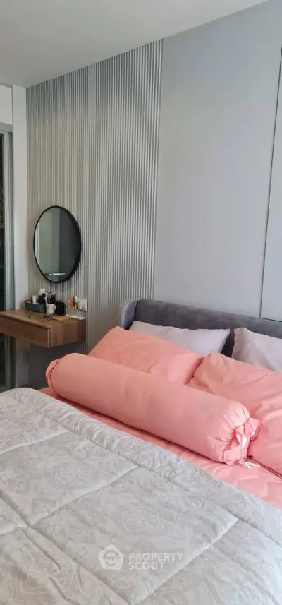 Modern bedroom with stylish decor and cozy bedding, featuring a round mirror and elegant wall paneling.