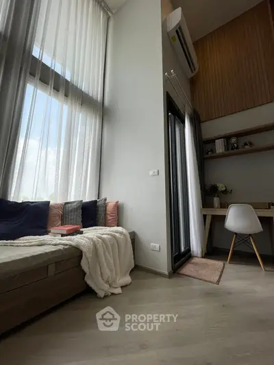 Modern living room with high ceilings and cozy seating area, featuring large windows and stylish decor.