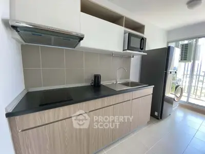 Modern kitchen with sleek cabinetry, induction cooktop, and large fridge in a bright apartment.