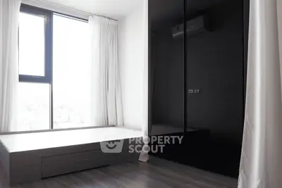 Modern minimalist bedroom with large window and sleek black wardrobe.