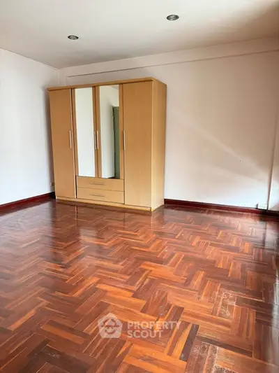 Spacious room with wooden wardrobe and polished parquet flooring