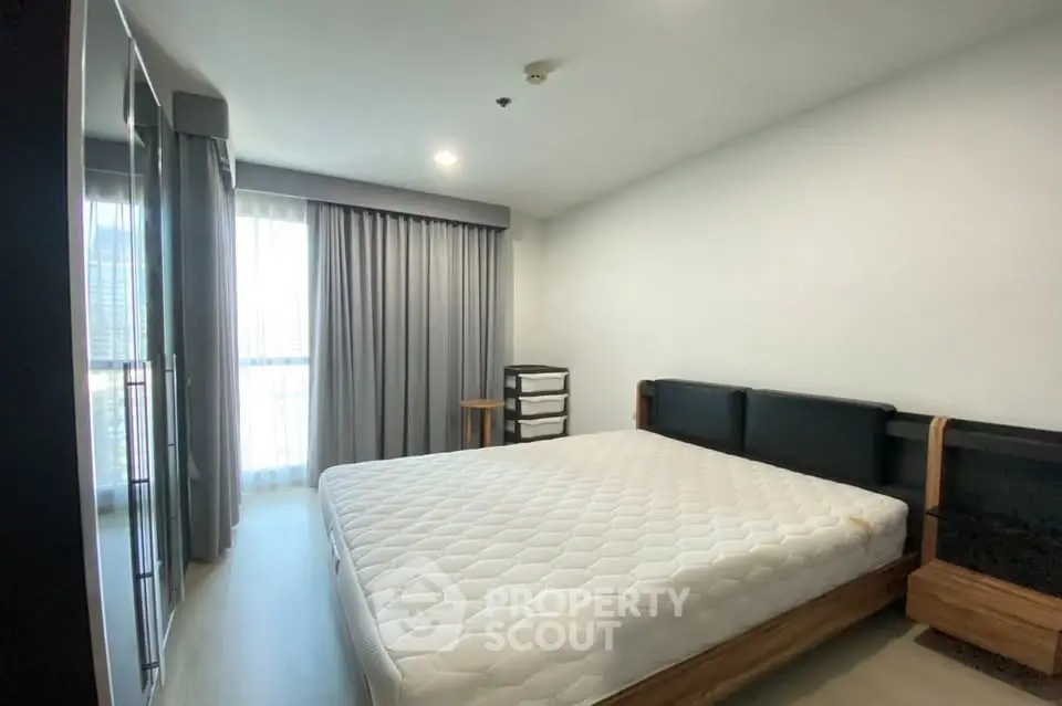 Spacious bedroom with large window and modern furnishings in a stylish apartment.