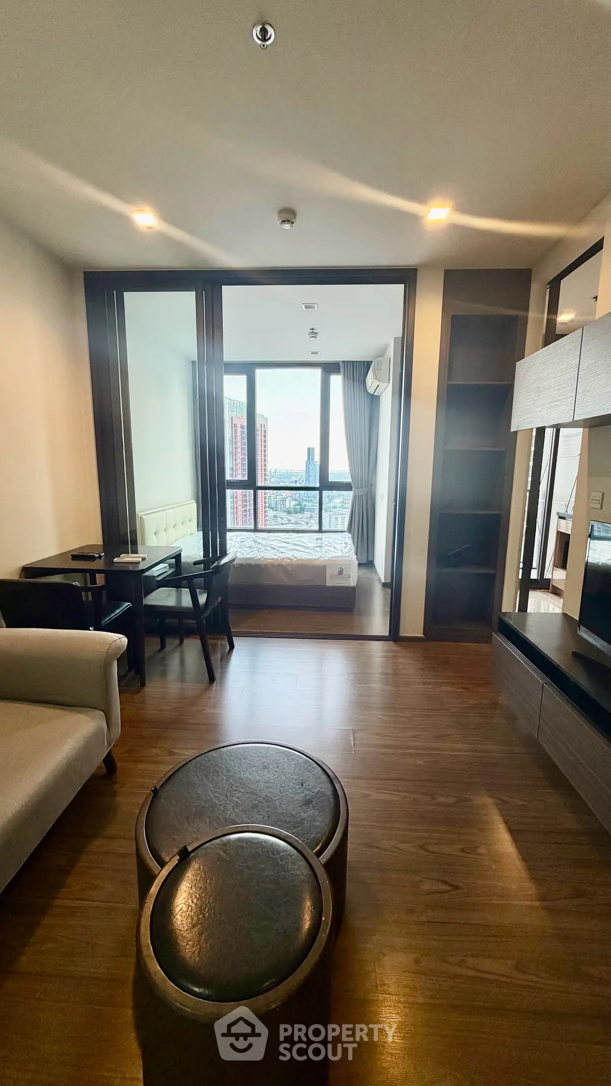 Modern living room with wooden flooring and city view, featuring cozy seating and stylish decor.
