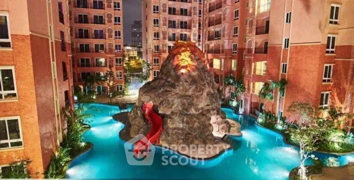 Luxurious apartment complex with stunning pool and rock feature at night.