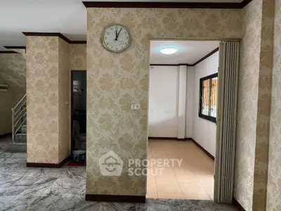 Spacious interior with elegant wallpaper and marble flooring, featuring a classic wall clock and open layout.