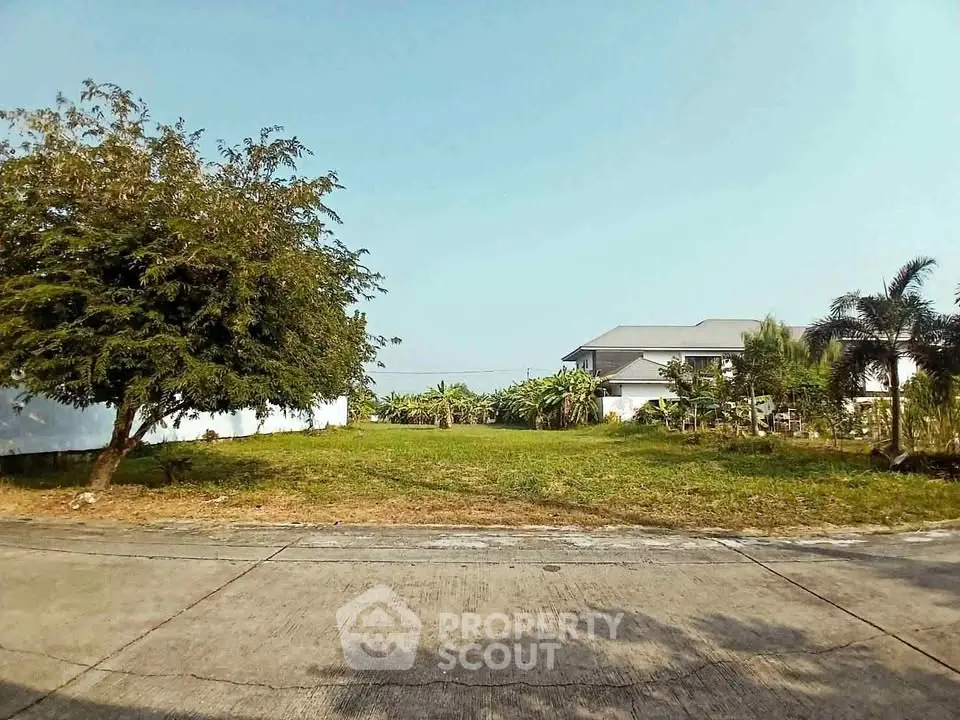 Spacious vacant lot with lush greenery and a modern house in the background, perfect for building your dream home.